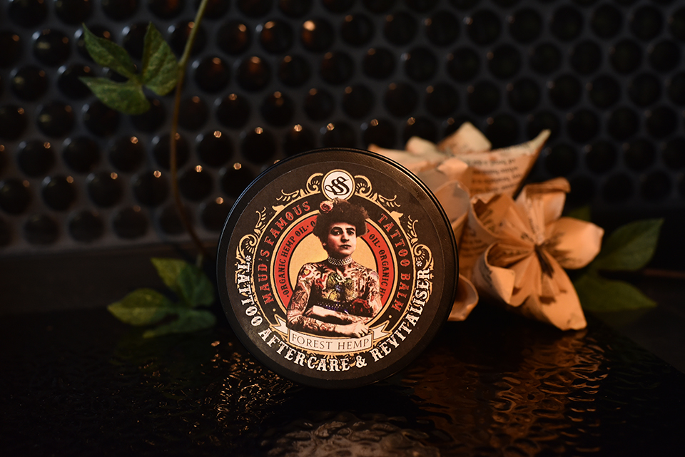 Maud's Famous Tattoo Balm, a black tin with a tattooed lady illustration on the lid